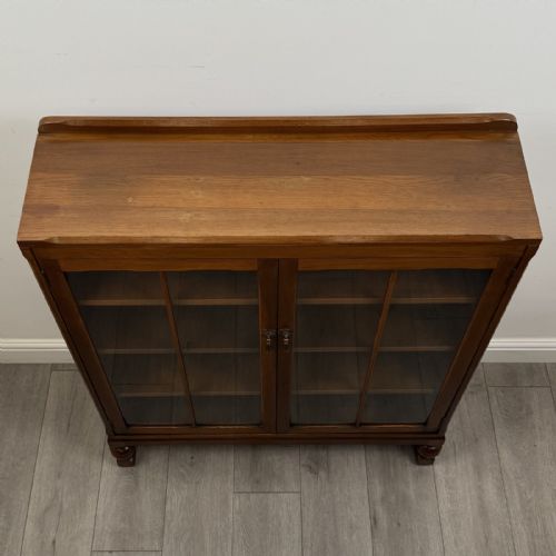 fig 9. A warm brown antique oak display cabinet featuring two glazed doors with wooden glazing bars and squat turned legs.