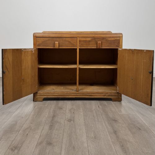 fig 1. A medium brown oak Art Deco sideboard featuring two drawers over two cabinet doors with long vertical carved wooden handles.