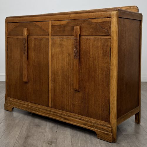 fig 2. A medium brown oak Art Deco sideboard featuring two drawers over two cabinet doors with long vertical carved wooden handles.