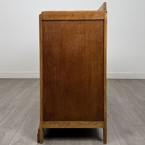 fig 3. A medium brown oak Art Deco sideboard featuring two drawers over two cabinet doors with long vertical carved wooden handles.