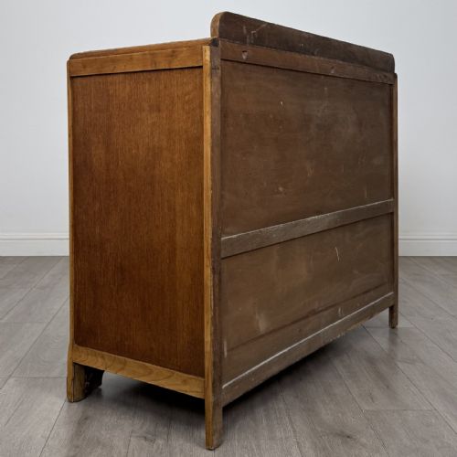 fig 4. A medium brown oak Art Deco sideboard featuring two drawers over two cabinet doors with long vertical carved wooden handles.