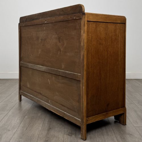 fig 6. A medium brown oak Art Deco sideboard featuring two drawers over two cabinet doors with long vertical carved wooden handles.