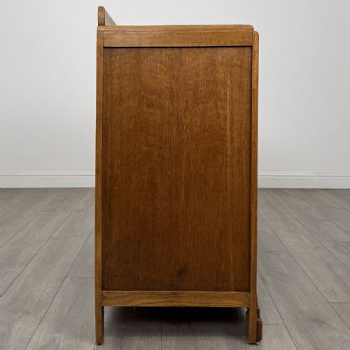 fig 7. A medium brown oak Art Deco sideboard featuring two drawers over two cabinet doors with long vertical carved wooden handles.
