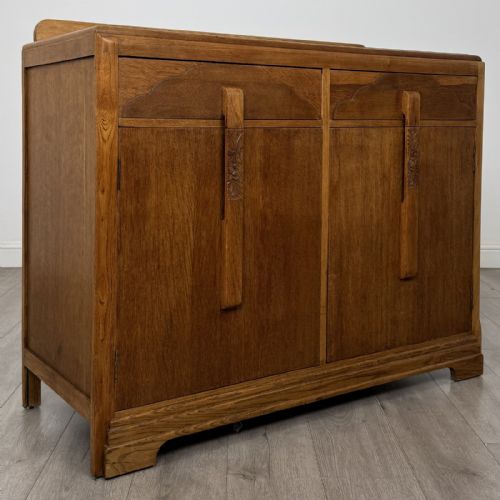 fig 8. A medium brown oak Art Deco sideboard featuring two drawers over two cabinet doors with long vertical carved wooden handles.