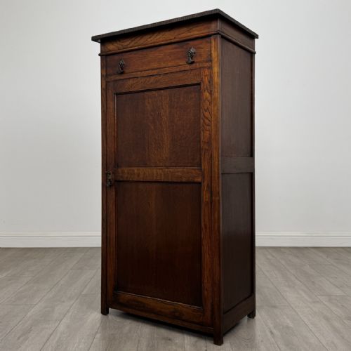 fig 2. A tall dark oak Edwardian storage cupboard featuring a lift-up top lid, panelled single door, and dark metal hardware.
