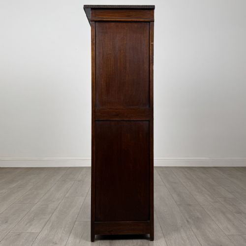fig 3. A tall dark oak Edwardian storage cupboard featuring a lift-up top lid, panelled single door, and dark metal hardware.