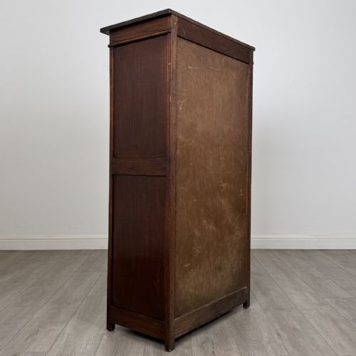 fig 4. A tall dark oak Edwardian storage cupboard featuring a lift-up top lid, panelled single door, and dark metal hardware.