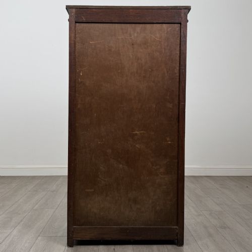fig 5. A tall dark oak Edwardian storage cupboard featuring a lift-up top lid, panelled single door, and dark metal hardware.
