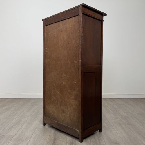 fig 6. A tall dark oak Edwardian storage cupboard featuring a lift-up top lid, panelled single door, and dark metal hardware.