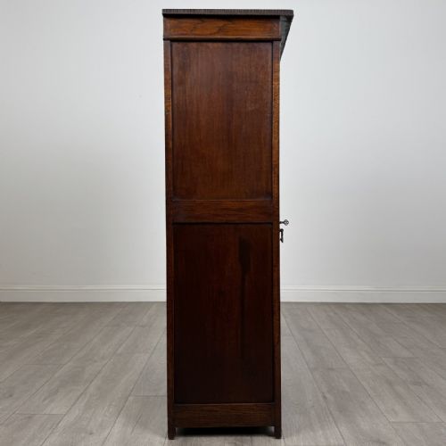 fig 7. A tall dark oak Edwardian storage cupboard featuring a lift-up top lid, panelled single door, and dark metal hardware.