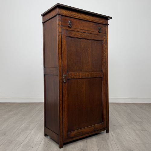 fig 8. A tall dark oak Edwardian storage cupboard featuring a lift-up top lid, panelled single door, and dark metal hardware.