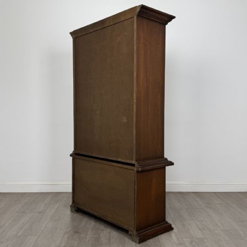 fig 7. A dark brown oak display cabinet featuring two glazed upper doors over two lower doors with carved geometric panels.