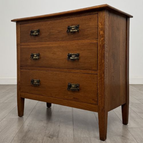 fig 1. An Edwardian golden oak chest of drawers featuring three full-width drawers with aged brass drop handles, supported by square tapered legs.