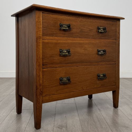 fig 6. An Edwardian golden oak chest of drawers featuring three full-width drawers with aged brass drop handles, supported by square tapered legs.