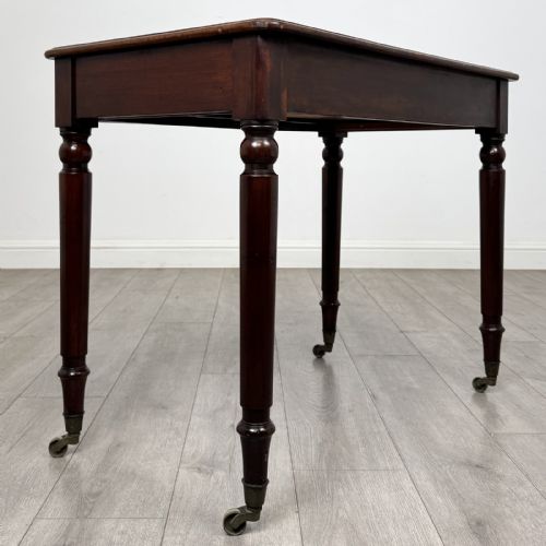 fig 3. Victorian mahogany writing table featuring a single frieze drawer with turned wooden knobs and four turned legs on brass castors.