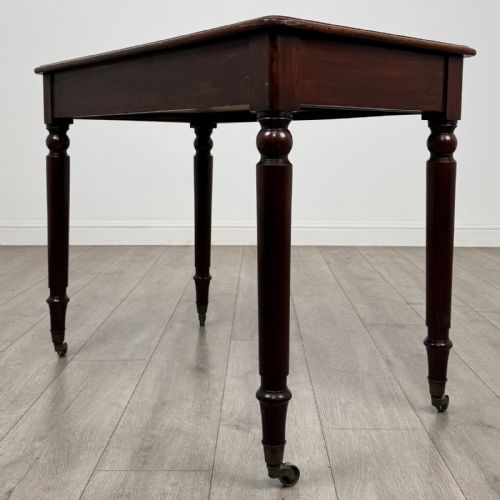 fig 5. Victorian mahogany writing table featuring a single frieze drawer with turned wooden knobs and four turned legs on brass castors.