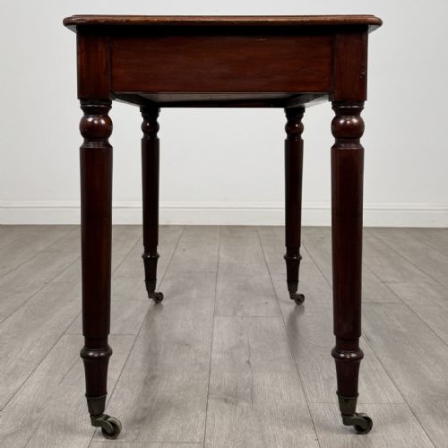 fig 6. Victorian mahogany writing table featuring a single frieze drawer with turned wooden knobs and four turned legs on brass castors.