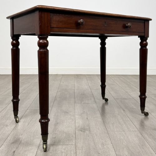 fig 7. Victorian mahogany writing table featuring a single frieze drawer with turned wooden knobs and four turned legs on brass castors.