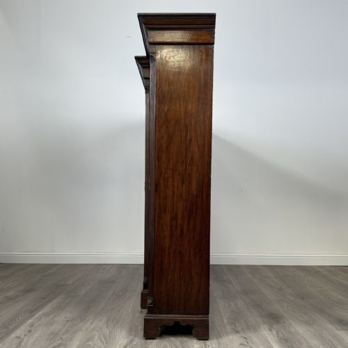 fig 3. A large dark oak display cabinet featuring a central glazed door with shelves, flanked by two solid panelled doors adorned with decorative brass strap hinges.