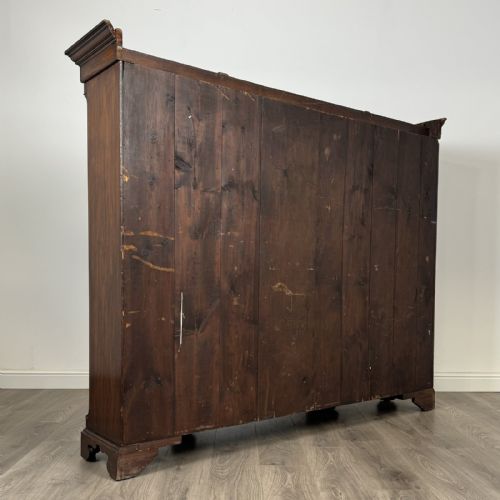 fig 4. A large dark oak display cabinet featuring a central glazed door with shelves, flanked by two solid panelled doors adorned with decorative brass strap hinges.