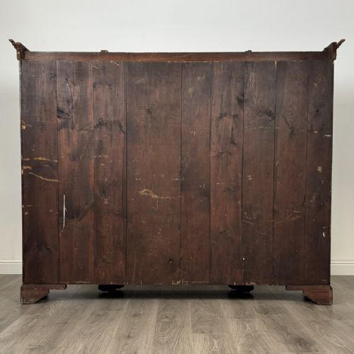 fig 5. A large dark oak display cabinet featuring a central glazed door with shelves, flanked by two solid panelled doors adorned with decorative brass strap hinges.