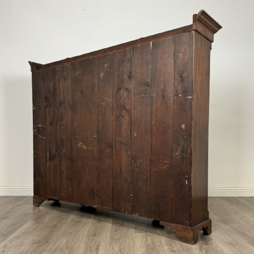 fig 6. A large dark oak display cabinet featuring a central glazed door with shelves, flanked by two solid panelled doors adorned with decorative brass strap hinges.
