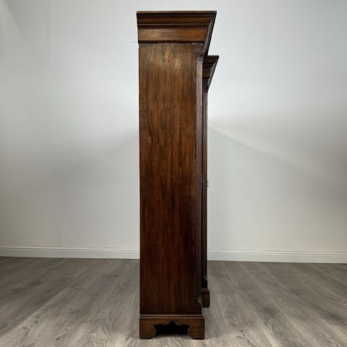 fig 7. A large dark oak display cabinet featuring a central glazed door with shelves, flanked by two solid panelled doors adorned with decorative brass strap hinges.