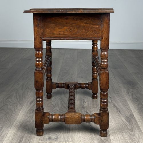 fig 2. An antique dark oak side table featuring a single drawer with brass drop handles, a scalloped apron, and bobbin-turned legs connected by matching stretchers.