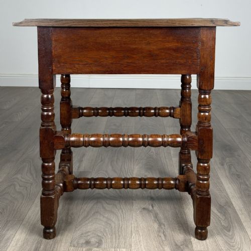 fig 4. An antique dark oak side table featuring a single drawer with brass drop handles, a scalloped apron, and bobbin-turned legs connected by matching stretchers.