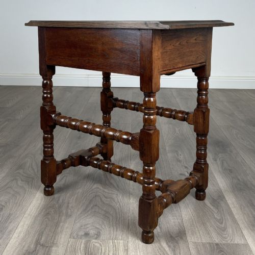 fig 5. An antique dark oak side table featuring a single drawer with brass drop handles, a scalloped apron, and bobbin-turned legs connected by matching stretchers.