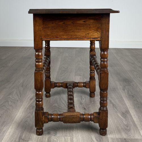 fig 6. An antique dark oak side table featuring a single drawer with brass drop handles, a scalloped apron, and bobbin-turned legs connected by matching stretchers.