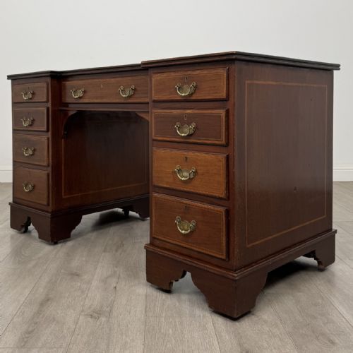 fig 1. A Victorian mahogany pedestal desk featuring a breakfront design, nine drawers with inlaid border details, brass swan-neck handles, and bracket feet.