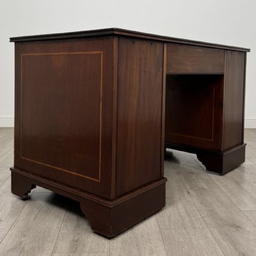 fig 3. A Victorian mahogany pedestal desk featuring a breakfront design, nine drawers with inlaid border details, brass swan-neck handles, and bracket feet.