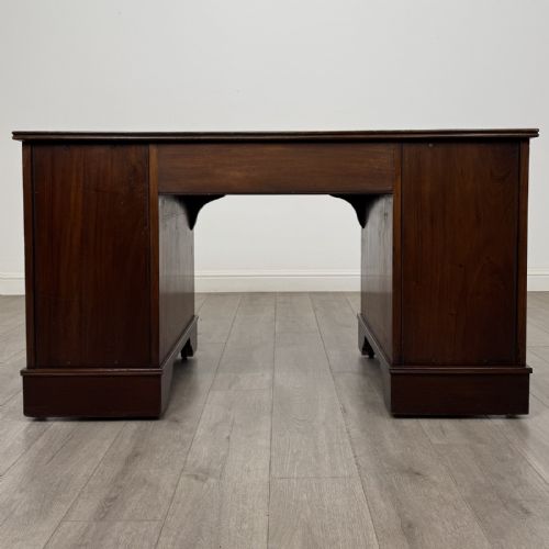 fig 4. A Victorian mahogany pedestal desk featuring a breakfront design, nine drawers with inlaid border details, brass swan-neck handles, and bracket feet.