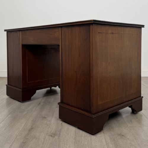 fig 5. A Victorian mahogany pedestal desk featuring a breakfront design, nine drawers with inlaid border details, brass swan-neck handles, and bracket feet.