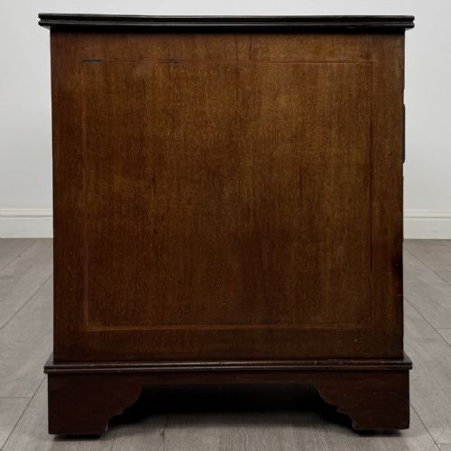 fig 6. A Victorian mahogany pedestal desk featuring a breakfront design, nine drawers with inlaid border details, brass swan-neck handles, and bracket feet.