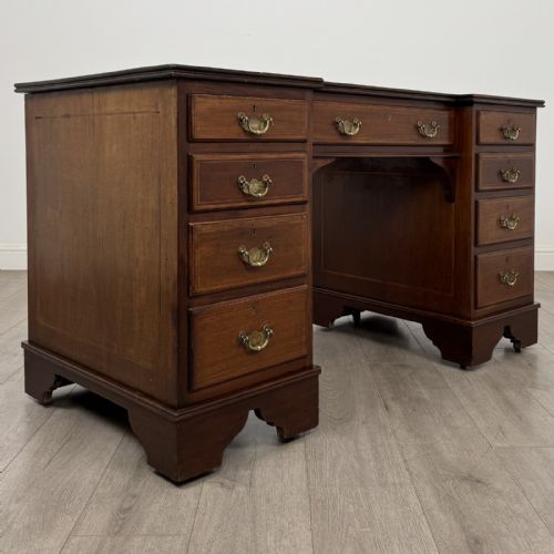 fig 7. A Victorian mahogany pedestal desk featuring a breakfront design, nine drawers with inlaid border details, brass swan-neck handles, and bracket feet.