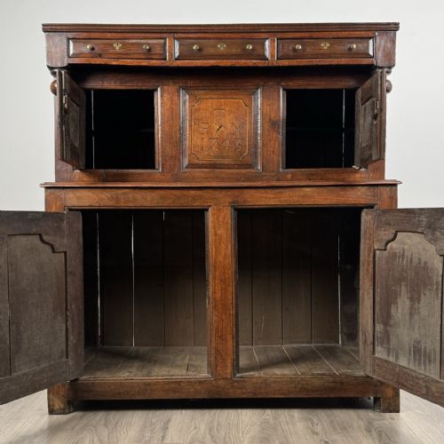 fig 1. An 18th-century Georgian dark oak Welsh deuddarn cupboard featuring carved upper panels dated 1743, turned drop pendants, and panelled cupboard doors.