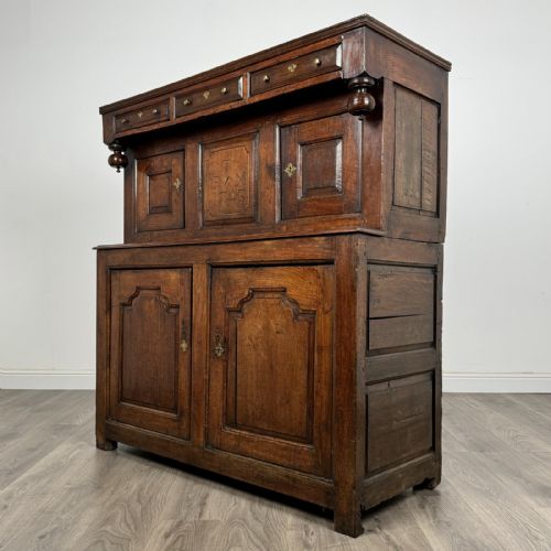 fig 2. An 18th-century Georgian dark oak Welsh deuddarn cupboard featuring carved upper panels dated 1743, turned drop pendants, and panelled cupboard doors.
