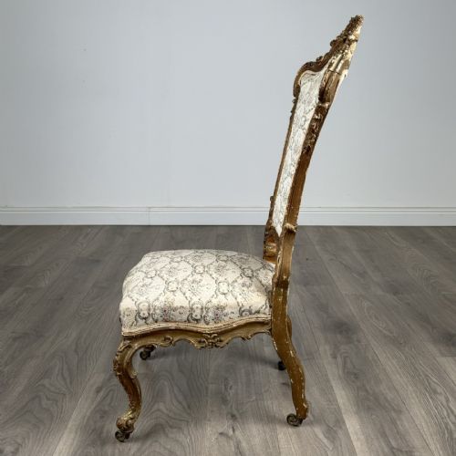 fig 1. An antique 19th-century French giltwood hall chair featuring a high upholstered backrest, ornate scroll carving, cabriole legs, and brass castors.