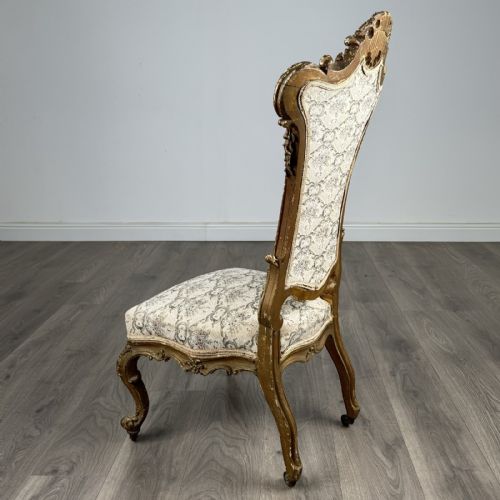 fig 2. An antique 19th-century French giltwood hall chair featuring a high upholstered backrest, ornate scroll carving, cabriole legs, and brass castors.