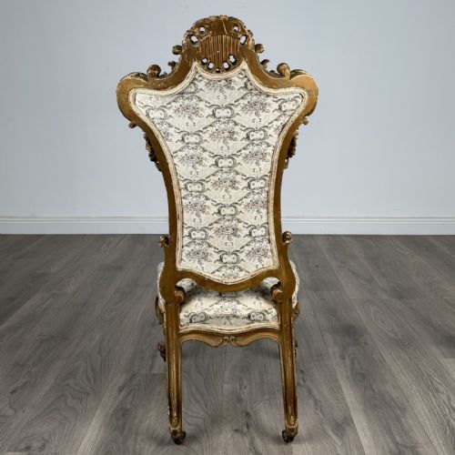 fig 3. An antique 19th-century French giltwood hall chair featuring a high upholstered backrest, ornate scroll carving, cabriole legs, and brass castors.
