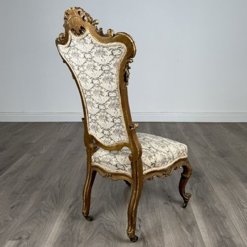 fig 4. An antique 19th-century French giltwood hall chair featuring a high upholstered backrest, ornate scroll carving, cabriole legs, and brass castors.