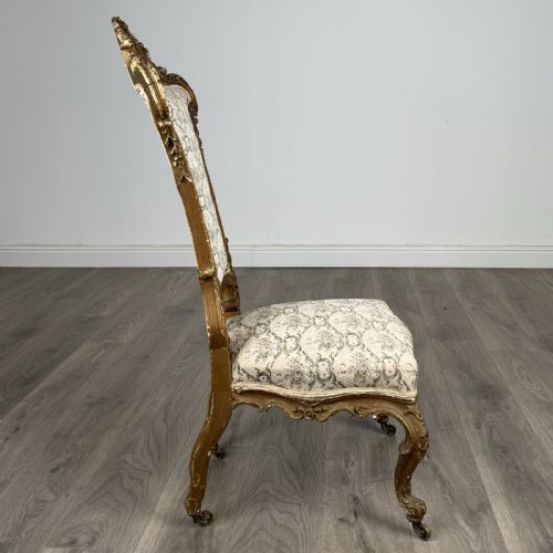 fig 5. An antique 19th-century French giltwood hall chair featuring a high upholstered backrest, ornate scroll carving, cabriole legs, and brass castors.