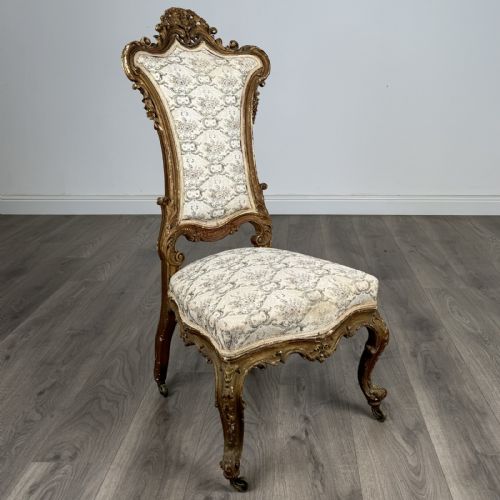 fig 6. An antique 19th-century French giltwood hall chair featuring a high upholstered backrest, ornate scroll carving, cabriole legs, and brass castors.