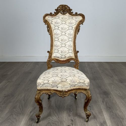 fig 7. An antique 19th-century French giltwood hall chair featuring a high upholstered backrest, ornate scroll carving, cabriole legs, and brass castors.