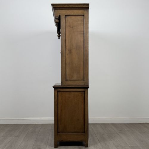 fig 3. A tall antique brown oak cupboard with carved spindle panels on the upper cabinet doors, brass butterfly hinges, two drawers, and a lower open alcove with a blue painted interior.