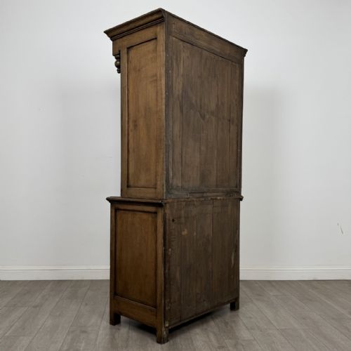 fig 4. A tall antique brown oak cupboard with carved spindle panels on the upper cabinet doors, brass butterfly hinges, two drawers, and a lower open alcove with a blue painted interior.
