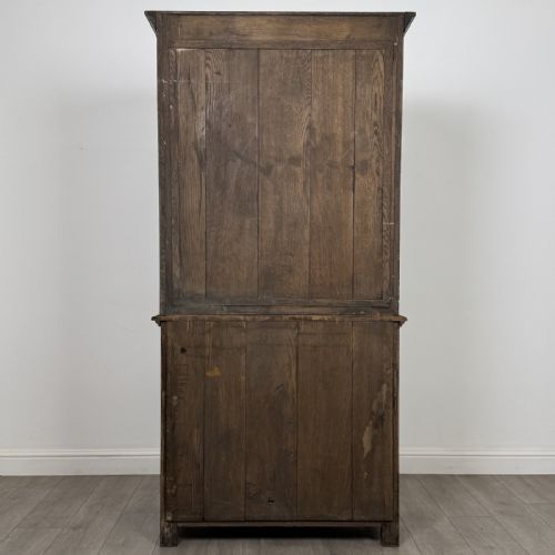 fig 5. A tall antique brown oak cupboard with carved spindle panels on the upper cabinet doors, brass butterfly hinges, two drawers, and a lower open alcove with a blue painted interior.