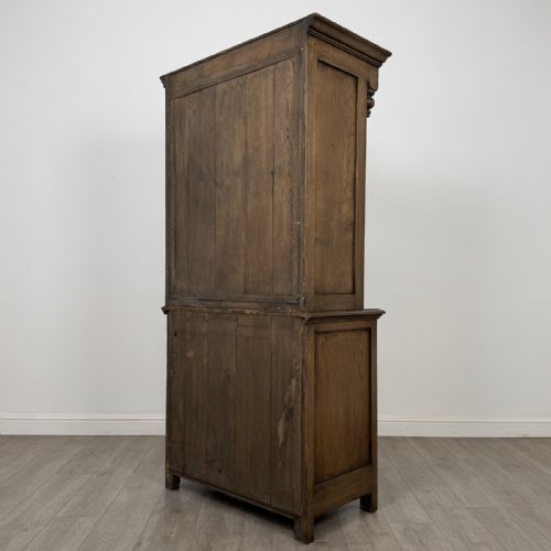 fig 6. A tall antique brown oak cupboard with carved spindle panels on the upper cabinet doors, brass butterfly hinges, two drawers, and a lower open alcove with a blue painted interior.